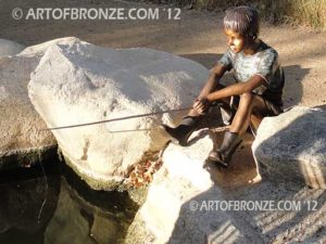 Fish n Hole bronze sculpture of young boy sitting and fishing