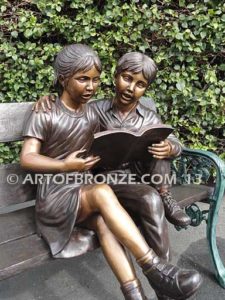 Friendship bronze sculpture of young girl and boy sitting on bench looking at book