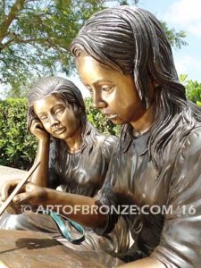 Big Sister Love closeup D bronze statue of two girls sitting and drawing