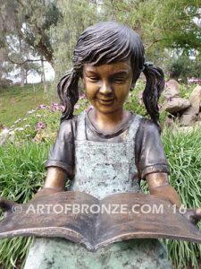 High Achiever bronze sculpture of girl wearing dress with pigtails sitting on log reading book