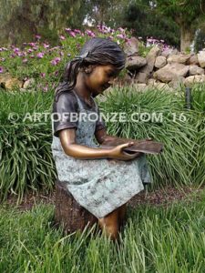 High Achiever bronze sculpture of girl wearing dress with pigtails sitting on log reading book