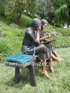 Big Sister side view A bronze statue of two girls sitting on bench drawing
