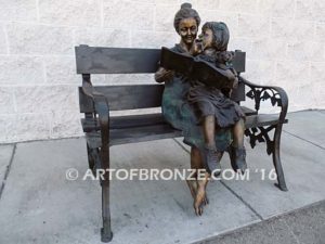 Bronze statue of adult woman reading book to young child on bronze bench