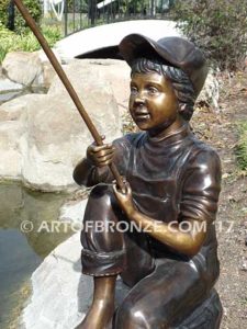 Gone Fishing bronze sculpture of girl sitting on rock fishing. Wearing overalls and baseball hat.