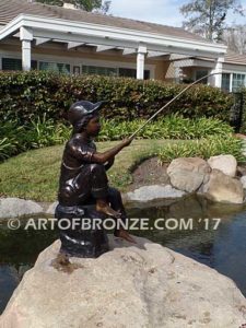 Gone Fishing bronze sculpture of girl sitting on rock fishing. Wearing overalls and baseball hat.