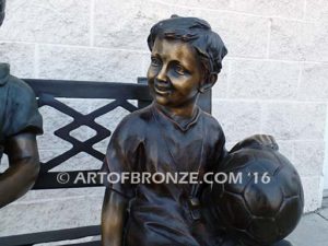 Special Day Together bronze sculpture of mother sitting on bench playing with her daughter, baby and soccer son