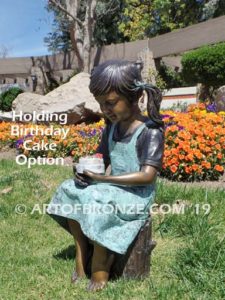 High Achiever bronze sculpture of girl wearing dress with pigtails sitting on log holding a birthday cake.