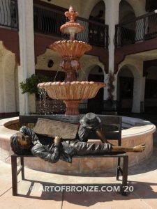 Boy napping on bench with newspaper bronzes statue in front of shopping center