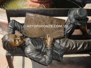 Boy napping on bench with newspaper bronzes statue in front of shopping center
