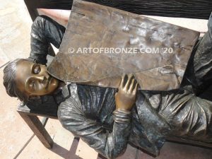 Boy napping on bench with newspaper bronzes statue in front of shopping center