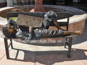 Boy napping on bench with newspaper bronzes statue in front of shopping center