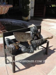 Boy napping on bench with newspaper bronzes statue in front of shopping center