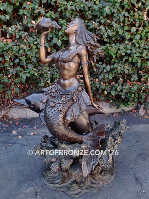 Bronze sculpture of mermaid riding dolphin blowing conch shell pond, pool or aquatic display