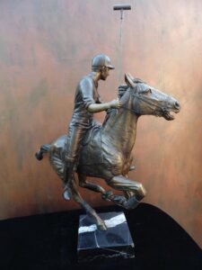 Downfield bronze sculpture of polo player riding his leaping polo pony attached to a marble base