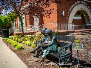 Friendship outdoor bronze garden sculpture of two children reading a book on bench