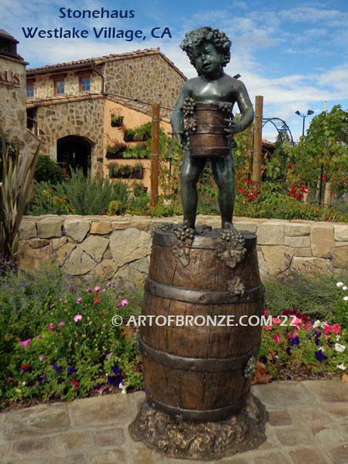 Harvest Time bronze statue of cherub boy standing on wine barrel with grapes on display at Stonehaus in Westlake Village, CA