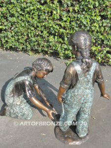 Helping Hand bronze statue of boy kneeling down and helping girl tie her shoelace