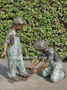 Helping Hand bronze statue of boy kneeling down and helping girl tie her shoelace