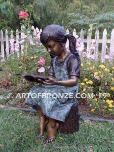 High Achiever bronze sculpture of girl wearing dress with pigtails sitting on log reading book