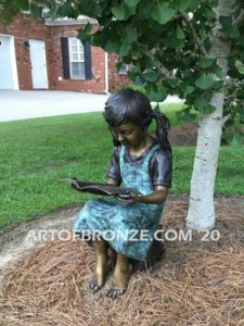 High Achiever bronze sculpture of girl wearing dress with pigtails sitting on log reading book
