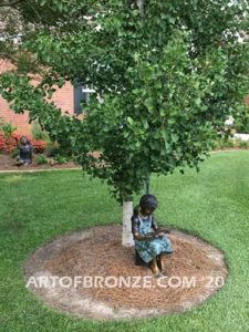 High Achiever bronze sculpture of girl wearing dress with pigtails sitting on log reading book