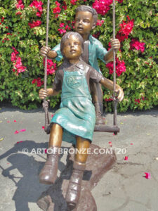 Higher & Higher outdoor bronze sculpture of boy pushing girl on swing