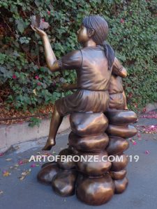 Loving Attention garden sculpture of kids sitting on rocks holding a dove in each hand