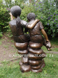 Loving Attention garden bronze statue of kids sitting on rocks holding a dove in each hand