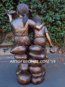 Loving Attention garden sculpture of kids sitting on rocks holding a dove in each hand