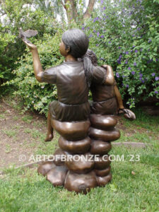 Loving Attention garden bronze statue of kids sitting on rocks holding a dove in each hand