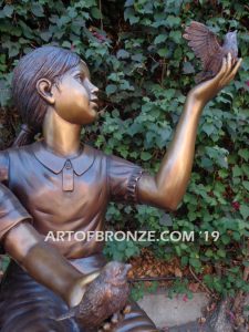 Loving Attention garden sculpture of kids sitting on rocks holding a dove in each hand