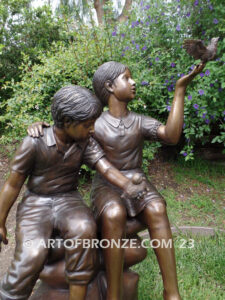 Loving Attention garden bronze statue of kids sitting on rocks holding a dove in each hand