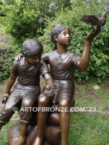 Loving Attention garden bronze statue of kids sitting on rocks holding a dove in each hand