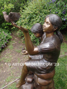 Loving Attention garden bronze statue of kids sitting on rocks holding a dove in each hand