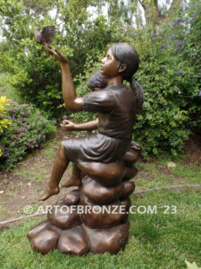 Loving Attention garden bronze statue of kids sitting on rocks holding a dove in each hand