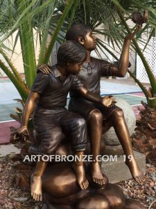 Loving Attention garden sculpture of kids sitting on rocks holding a dove in each hand