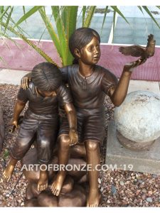 Loving Attention garden sculpture of kids sitting on rocks holding a dove in each hand