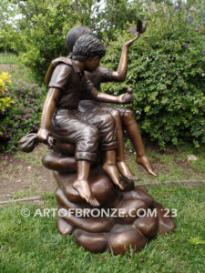 Loving Attention garden bronze statue of kids sitting on rocks holding a dove in each hand