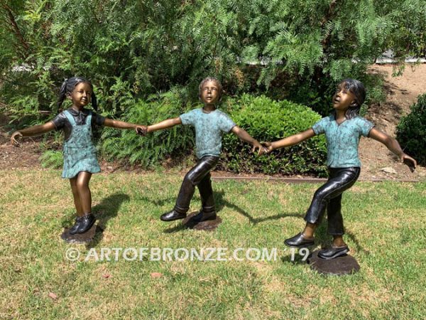 Sing Along wonderful outdoor bronze sculpture featuring three young kids holding hands and dancing