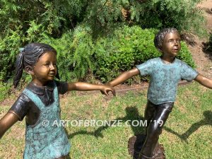 Sing Along wonderful outdoor bronze sculpture featuring three young kids holding hands and dancing