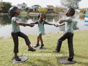 Sing Along wonderful outdoor bronze sculpture featuring three young kids holding hands and dancing
