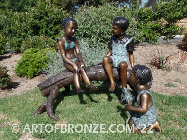 Telling Stories wonderful outdoor bronze sculpture featuring three children playing together on bronze log