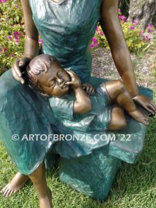 Mothers Love bronze sculpture of seated woman sitting on bench with young boy sleeping on her lap