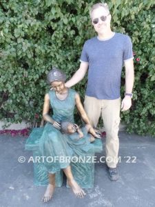 Mothers Love bronze sculpture of seated woman sitting on bench with young boy sleeping on her lap