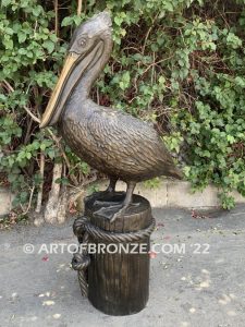 Home Pier bronze statue of playful pelican on bronze piling with rope