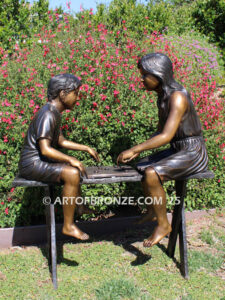 bronze sculpture of boy and girl sitting bench playing checkers