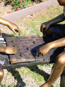 bronze sculpture of boy and girl sitting bench playing checkers