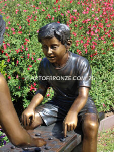 bronze sculpture of boy and girl sitting bench playing checkers